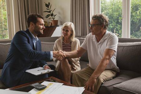 Front view of active senior Caucasian man shaking hands with real estate agent in living room at home